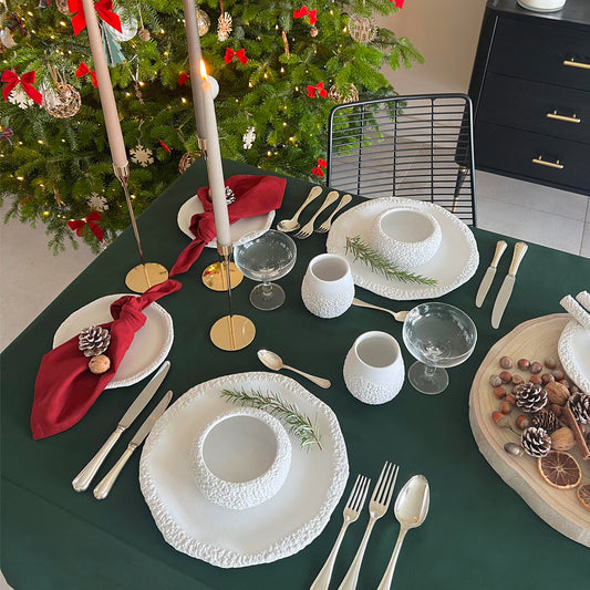 Christmas festive table with white dinnerware, green linen table cloth and burgundy linen napkins with candles