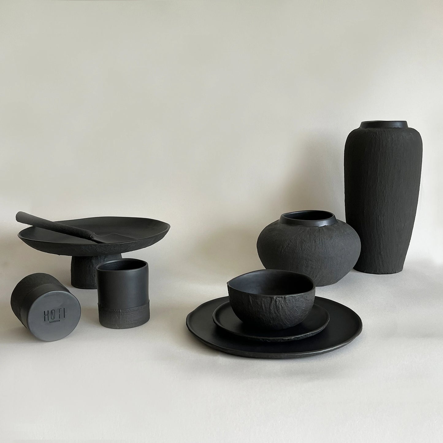 Set of matte black ceramic dishes and vases designed with linen raw organic texture.