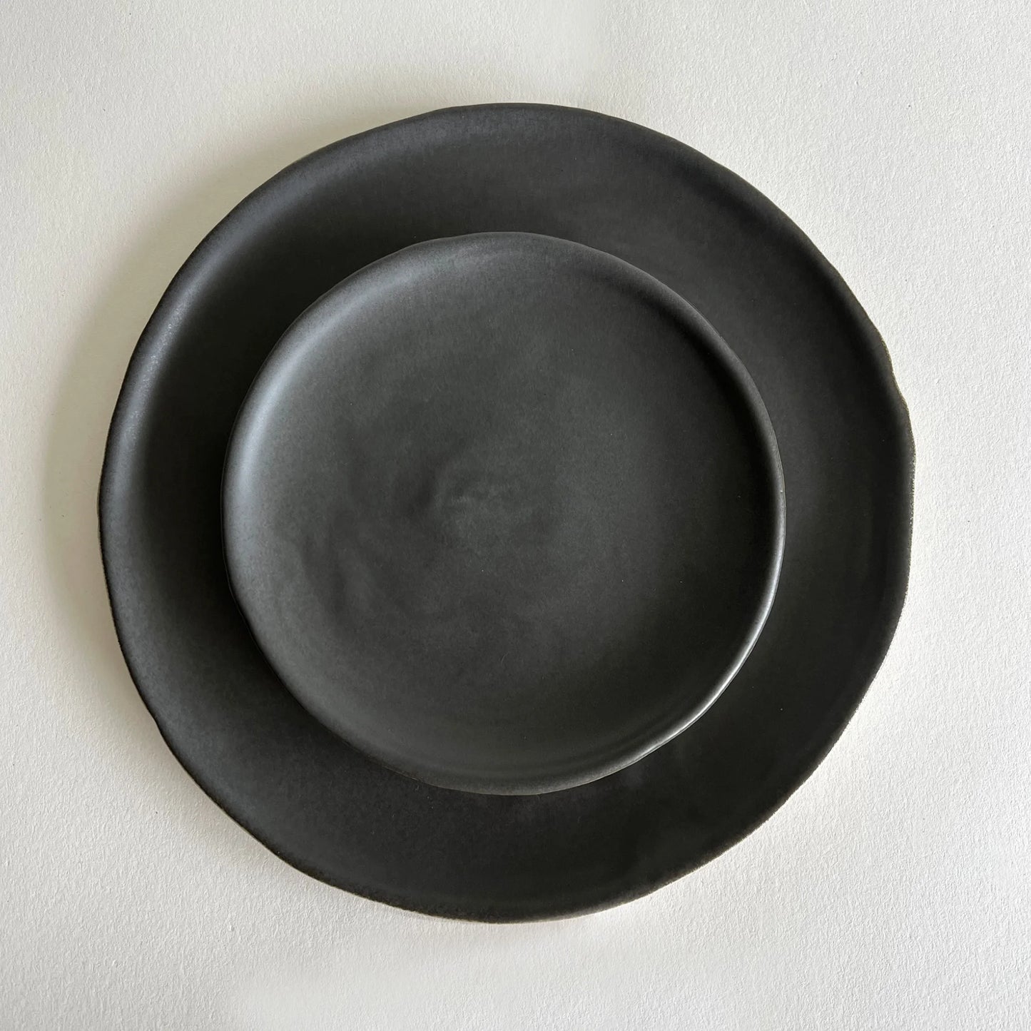 A set of two matte charcoal ceramic dinner and salad plate, organically formed.