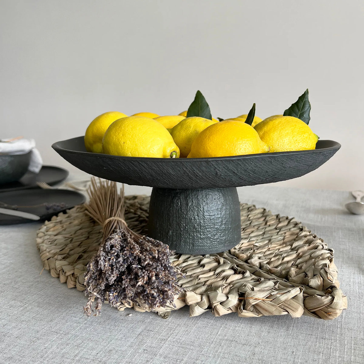 Black matte textured ceramic pedestal tray or platter with lemons on a textured surface