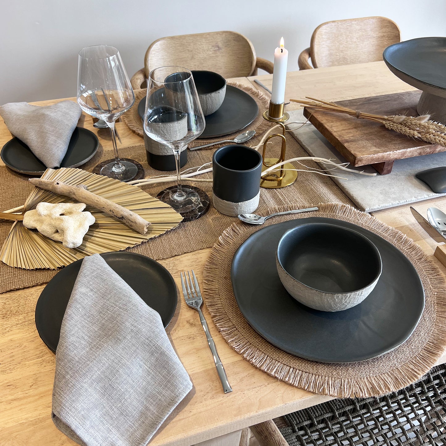 Dining table set with grey and beige ceramic plates, glasses, cups and cutlery on a wooden table.