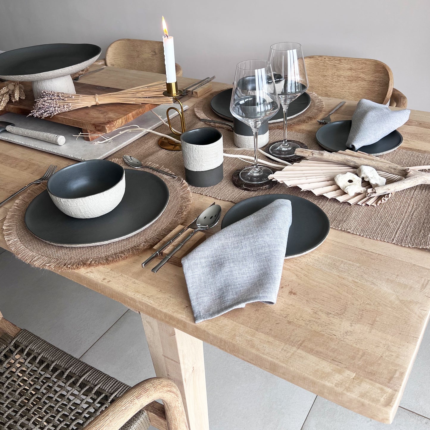 Dining table set with beige and grey ceramic plates, bowls, cups, grey napkins, and wooden chairs.