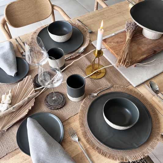 Dining table setting with grey ceramic plates, bowls, cups and gold candle holders.