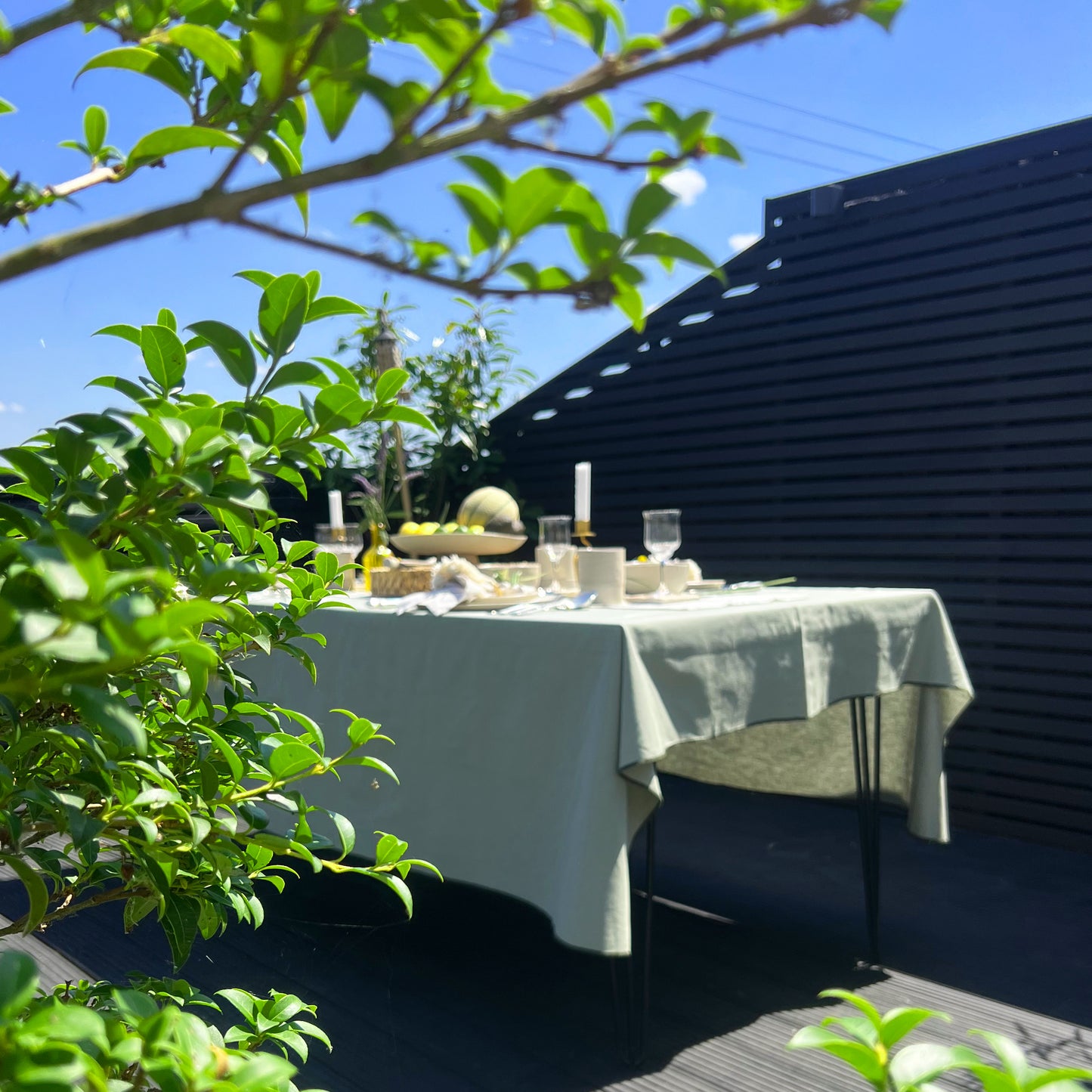 Outdoor table setting with a white tablecloth, glasses, and a candle under a clear blue sky.