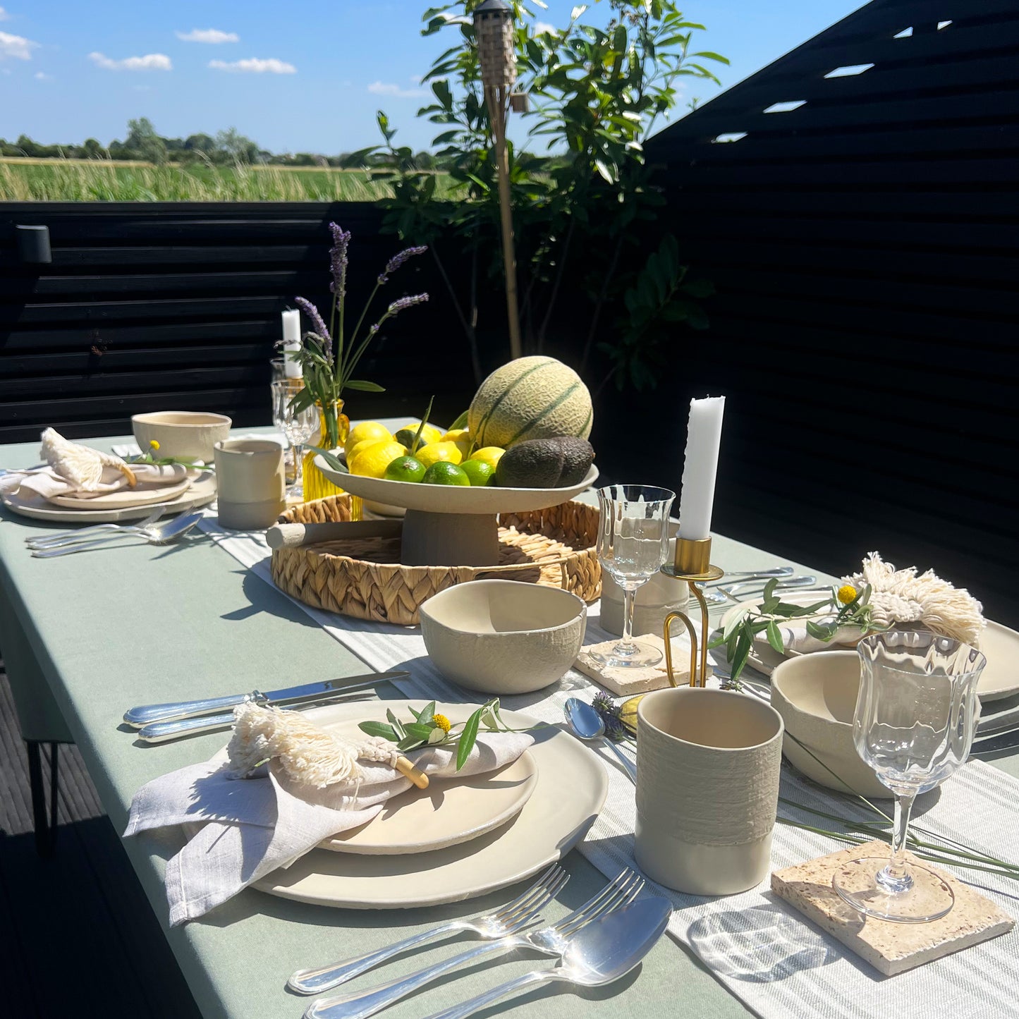 Outdoor table setting with plates, cups, and cutlery on a sage green tablecloth.