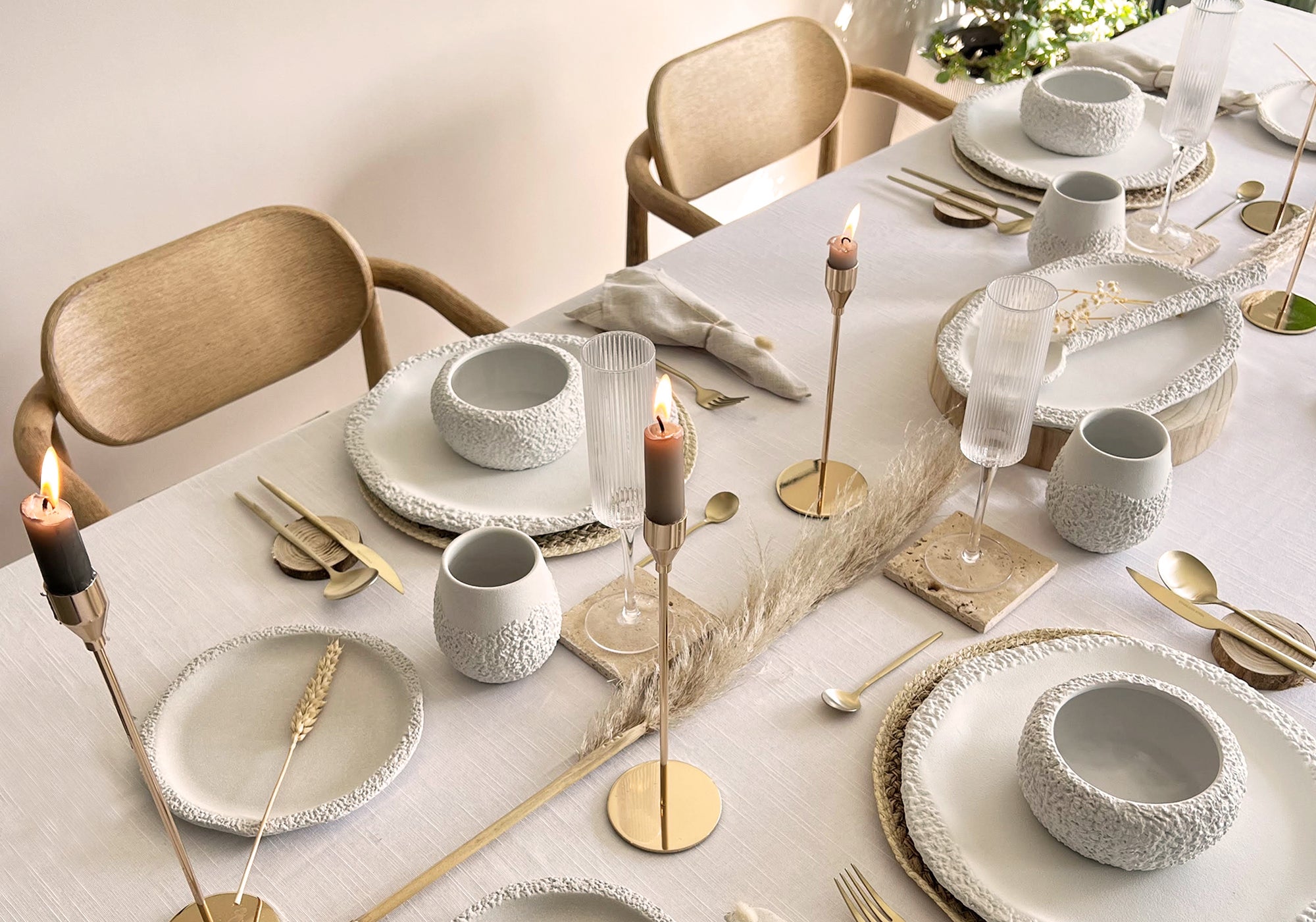 Elegant dining table setting with white ceramic dinnerware set, gold cutlery, and candles on a white linen tablecloth