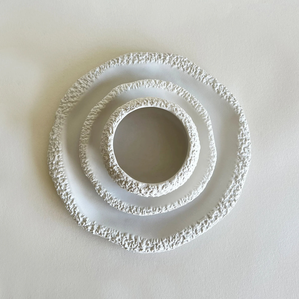Three textured white ceramic plates and bowls of varying sizes, with organic stone texture