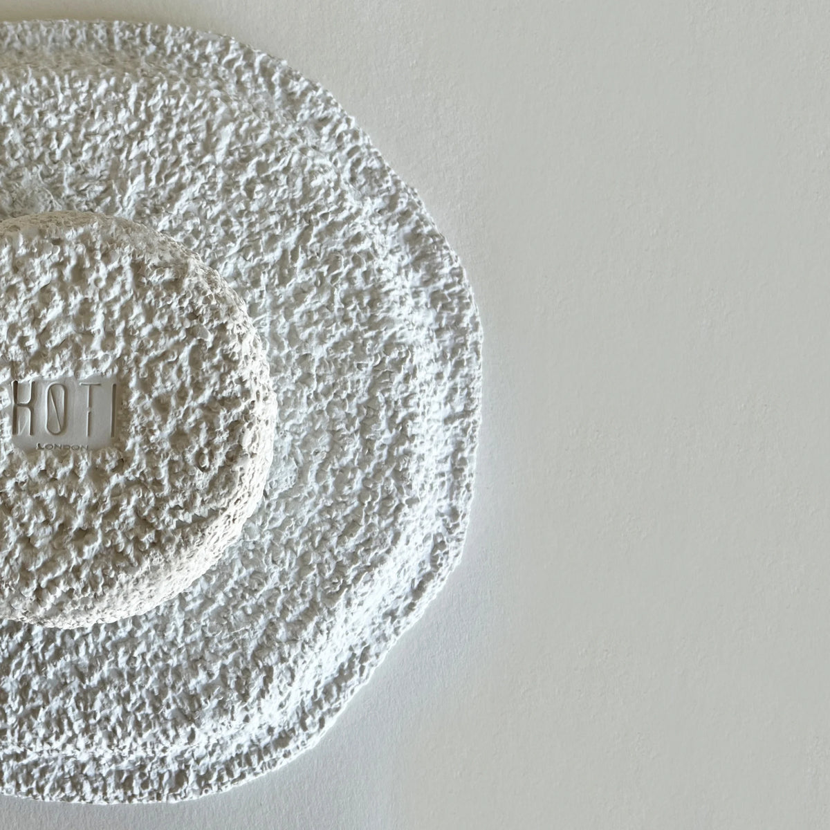 A close-up of a textured white ceramic or stone dining large plate and bowls with embossed brand logo