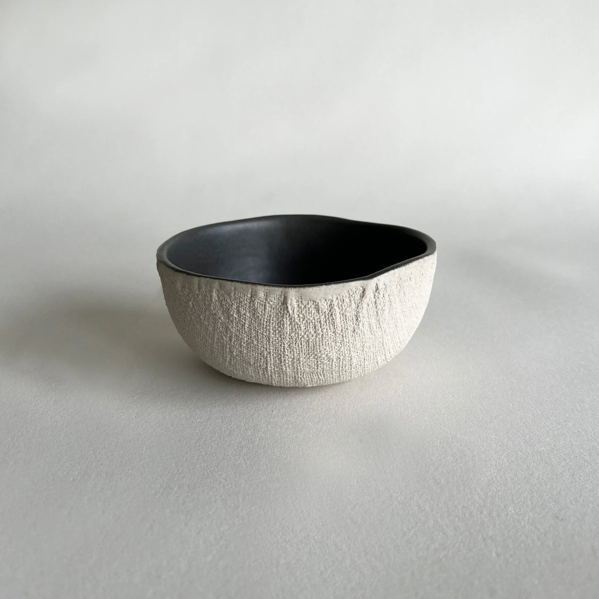 Cereal or soup handmade ceramic bowl in matte charcoal colour, contrasted with beige organic texture.