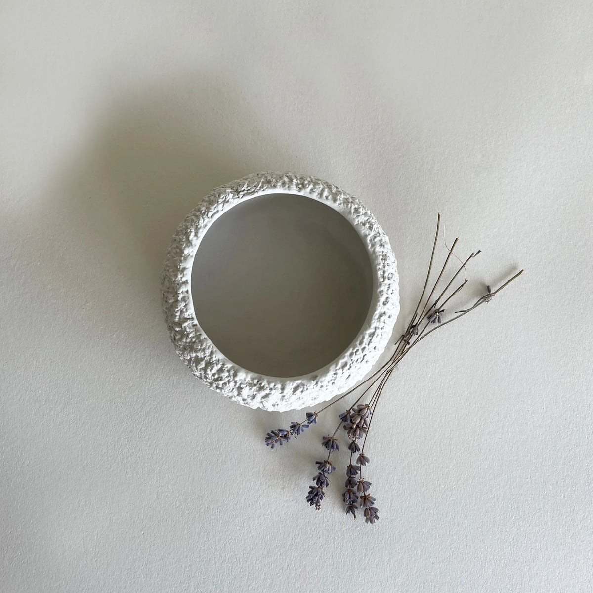 A round, textured white ceramic soup and breakfast owl with a rough, pebble surface, shown from a top down view on a neutral off white background with dried lavender sprigs.