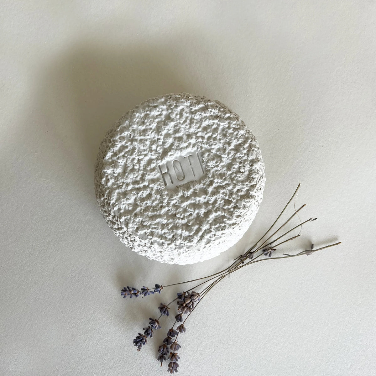 A close up of round, textured white cup with stone organic finish, showcasing the brand logo in the middle.
