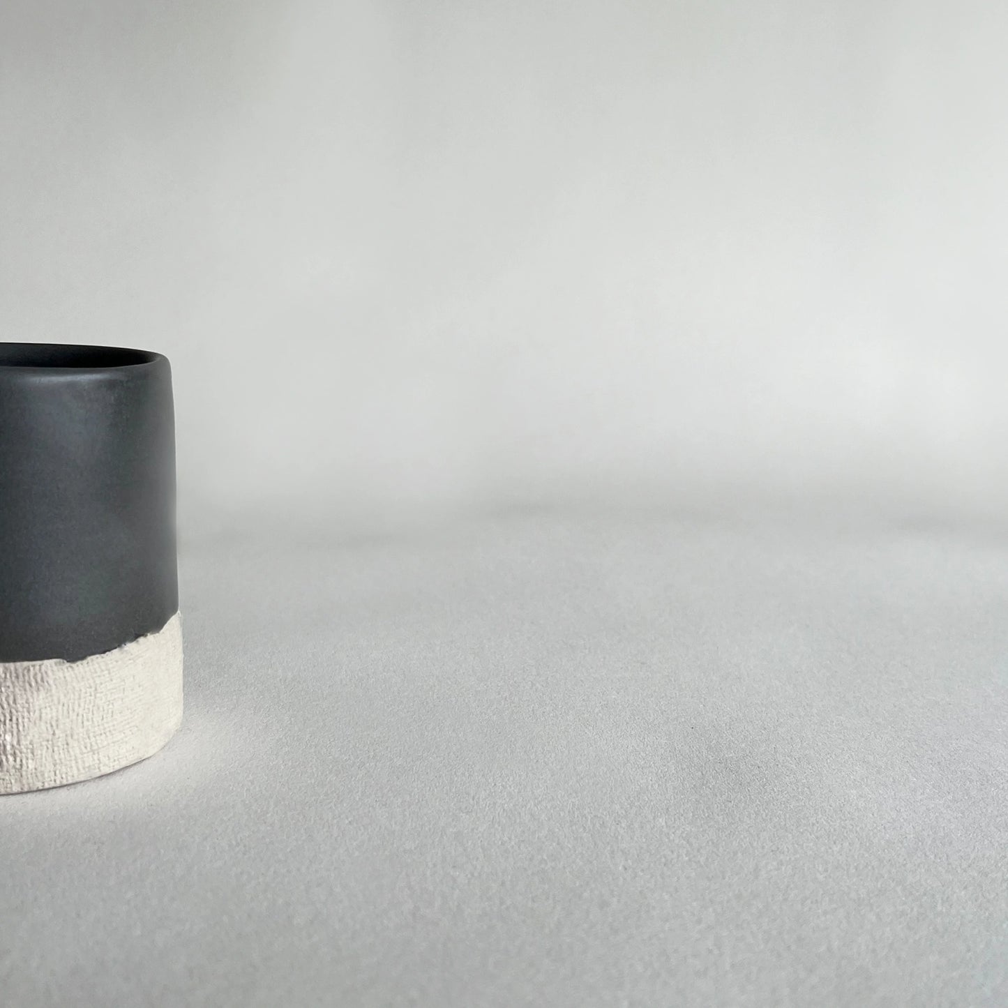 Details of organic handmade ceramic cup, in satin charcoal colour contrasted with beige organic finish.