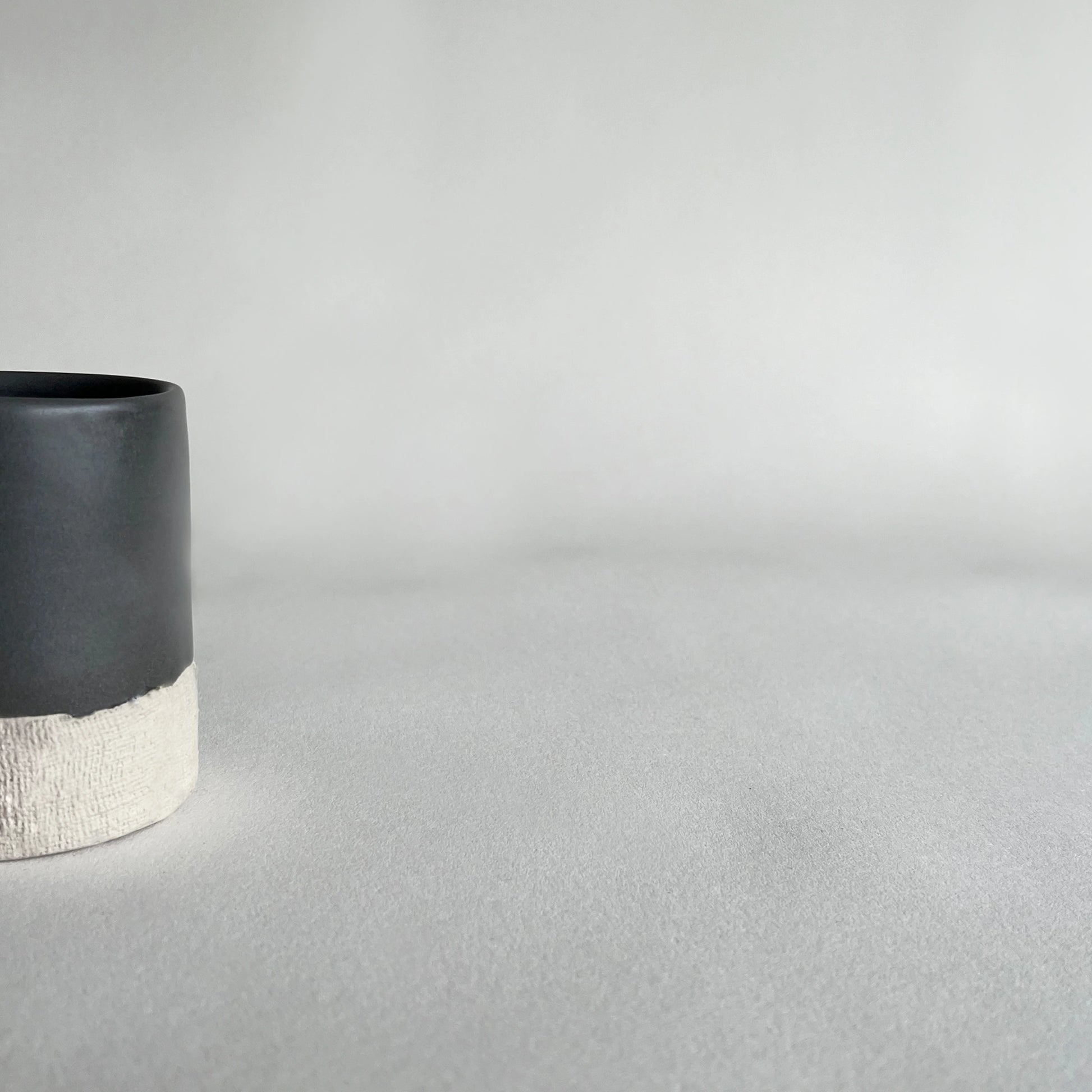 Details of organic handmade ceramic cup, in satin charcoal colour contrasted with beige organic finish.