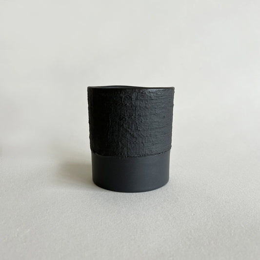 A minimalist black matte ceramic cup with a textured, ribbed upper half and a smooth matte lower half.