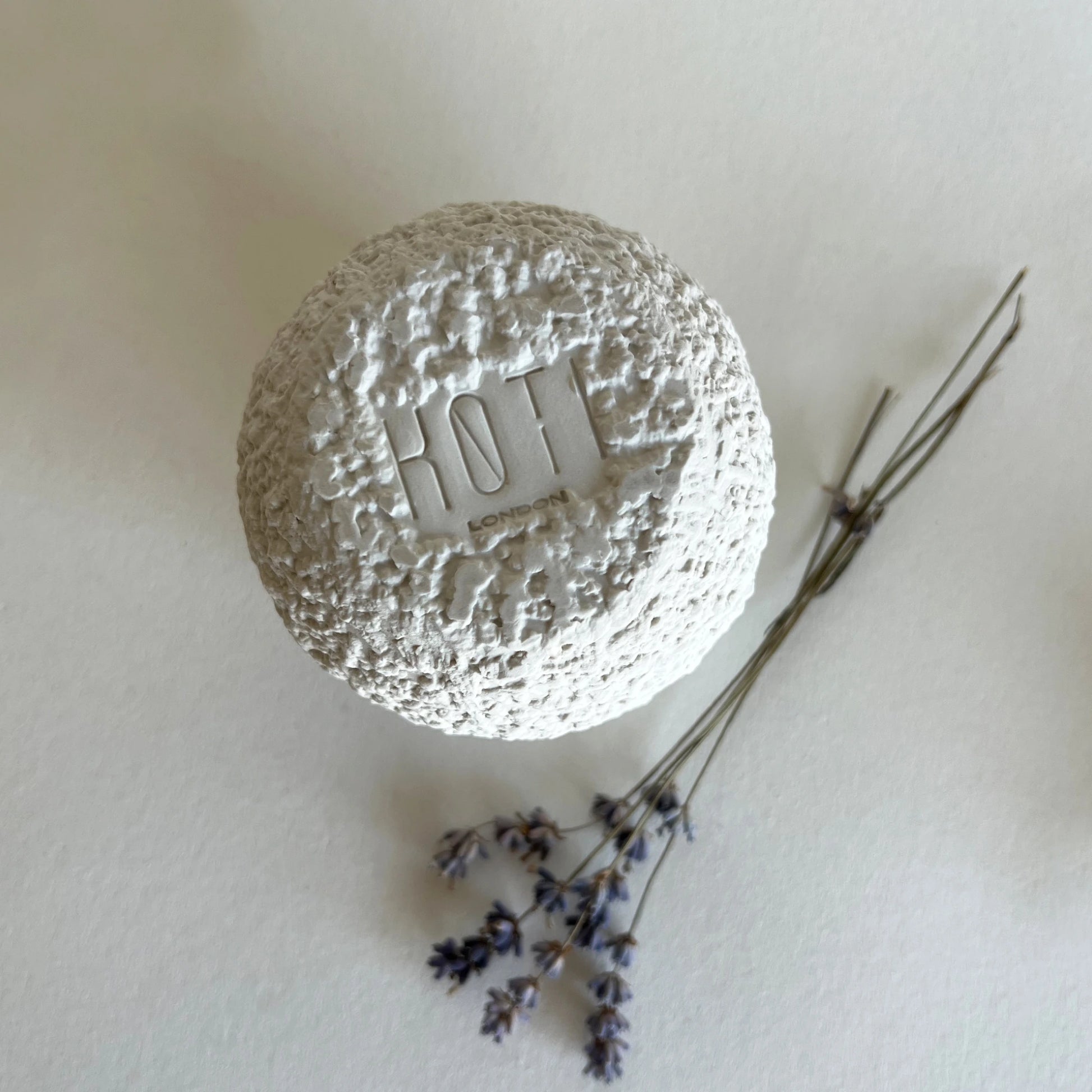 A close up of textured white ceramic coffee mug styled on a light beige background with dried lavender sprigs.