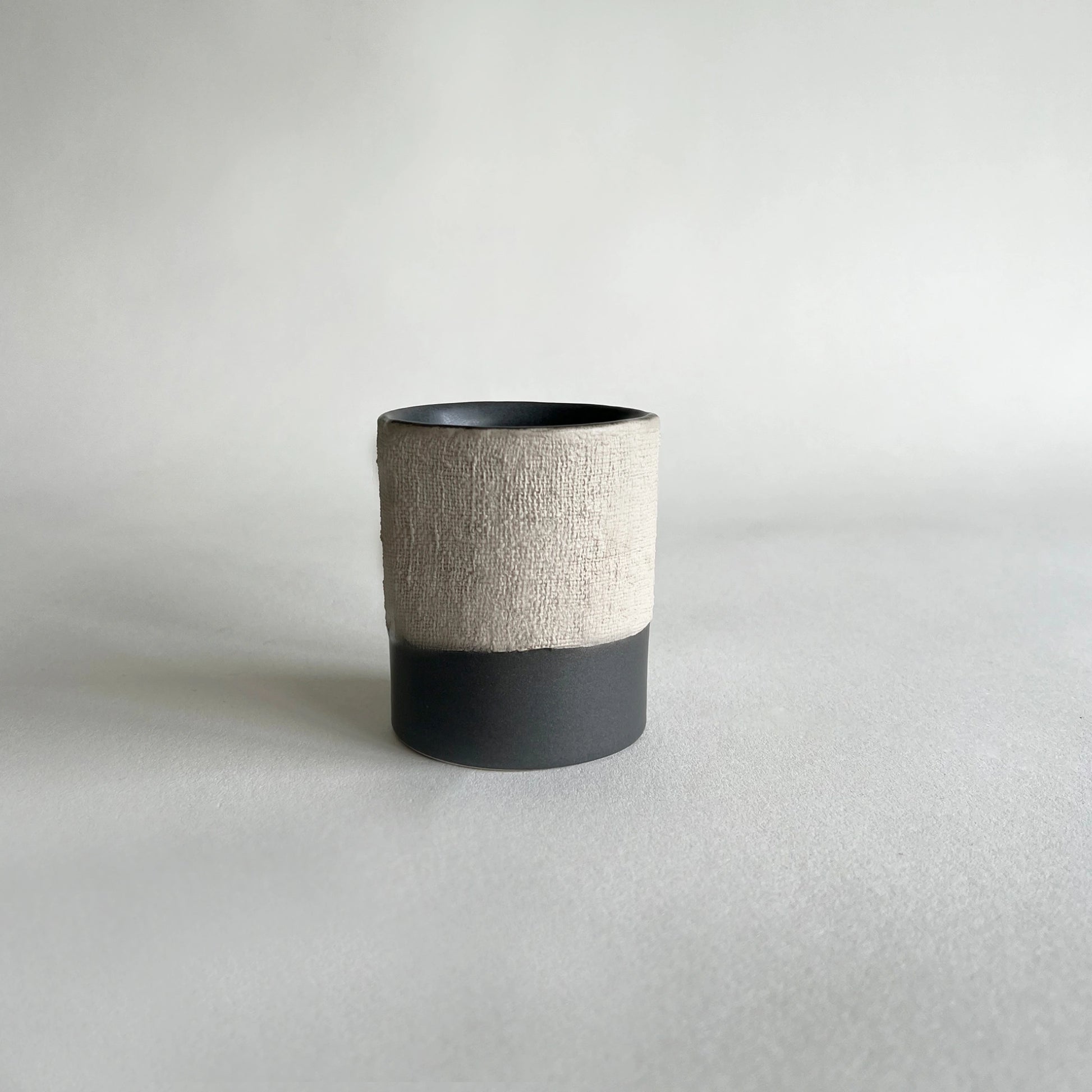 Handmade minimalistic ceramic coffee cup and mug, in matte charcoal colour, contrasted with beige rustic finish.