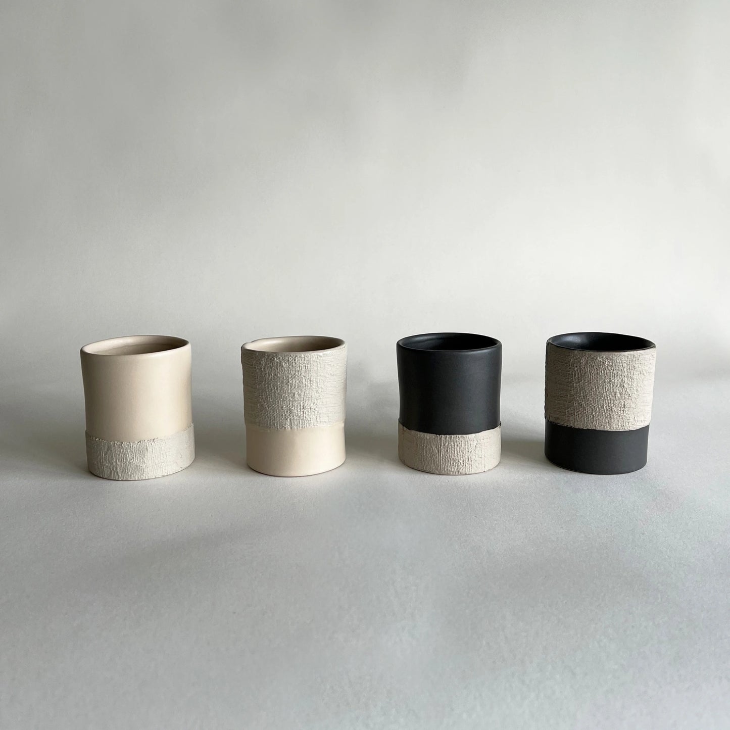 Four large ceramic cups  The cups have a matte finish with a two-tone design: one half is a warm cream/beige, and the other half is a textured light grey or off-white.