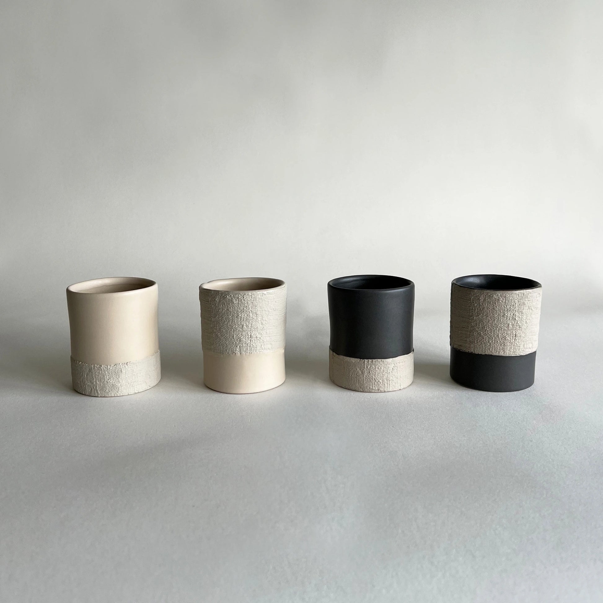 Four large ceramic cups  The cups have a matte finish with a two-tone design: one half is a warm cream/beige, and the other half is a textured light grey or off-white.