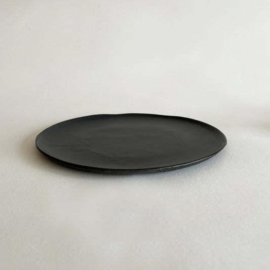 Large pizza ceramic plate in matte black finish with slightly irregular and organic edges. 