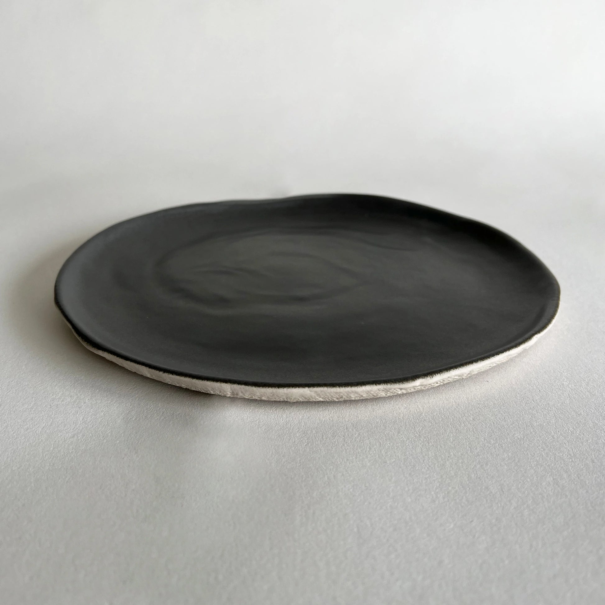 Large ceramic dinner plate in matte charcoal colour, with contrasted beige texture.