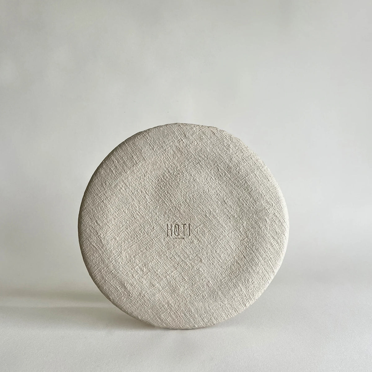 A round, textured large dinner plate in ceramic, showcasing raw and organic texture applied by hand, in beige matte colour. 