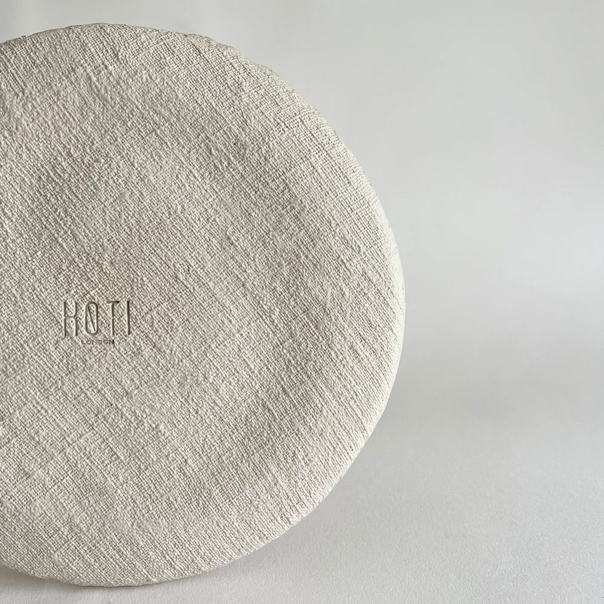 A close-up of a round, textured beige large ceramic dinner plate, applying jute texture. 