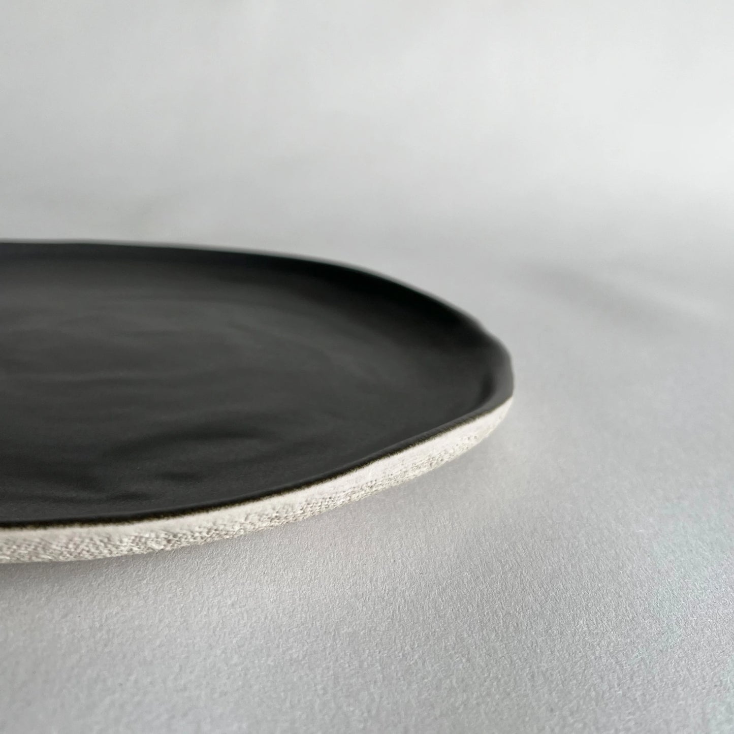 Close up of large ceramic dinner plate in matte charcoal colour in organic form. 