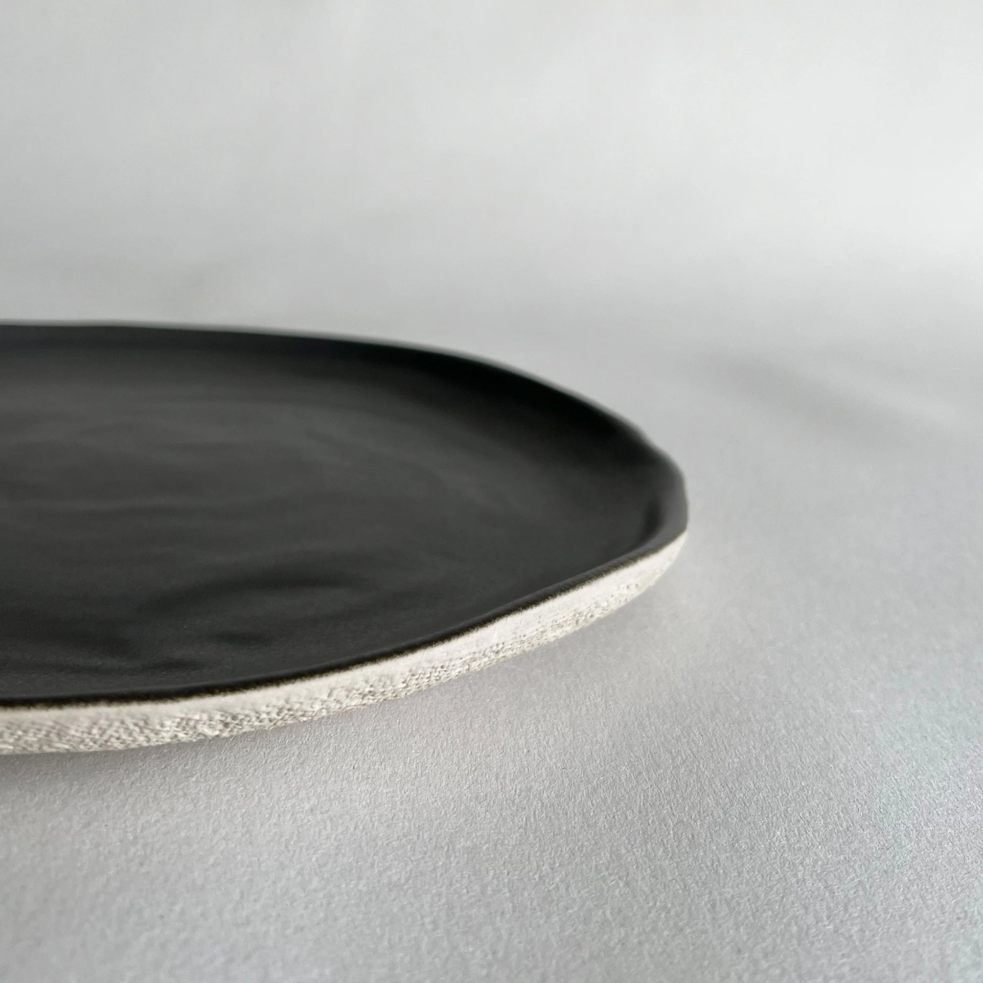 Close up of large ceramic dinner plate in matte charcoal colour in organic form. 