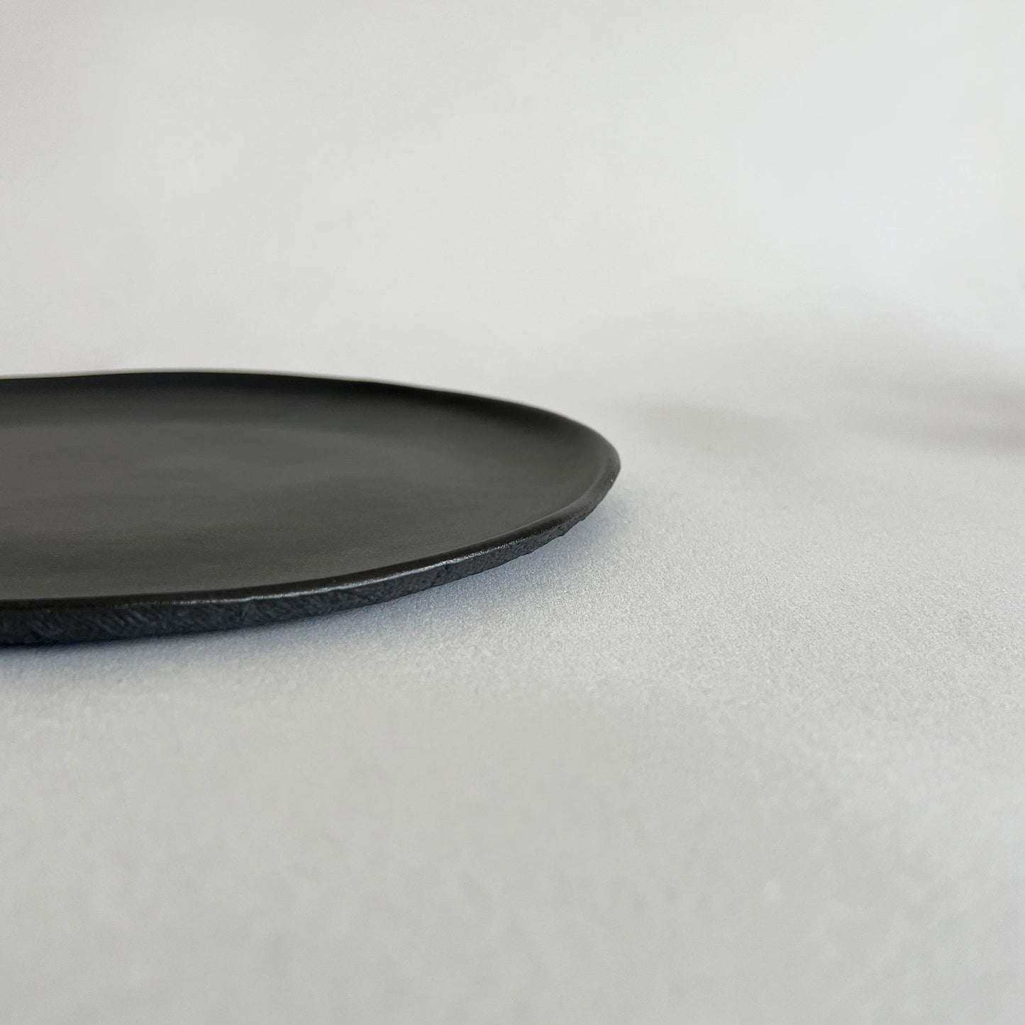 A minimalist black ceramic pizza plate with a matte finish and a slightly textured rim.