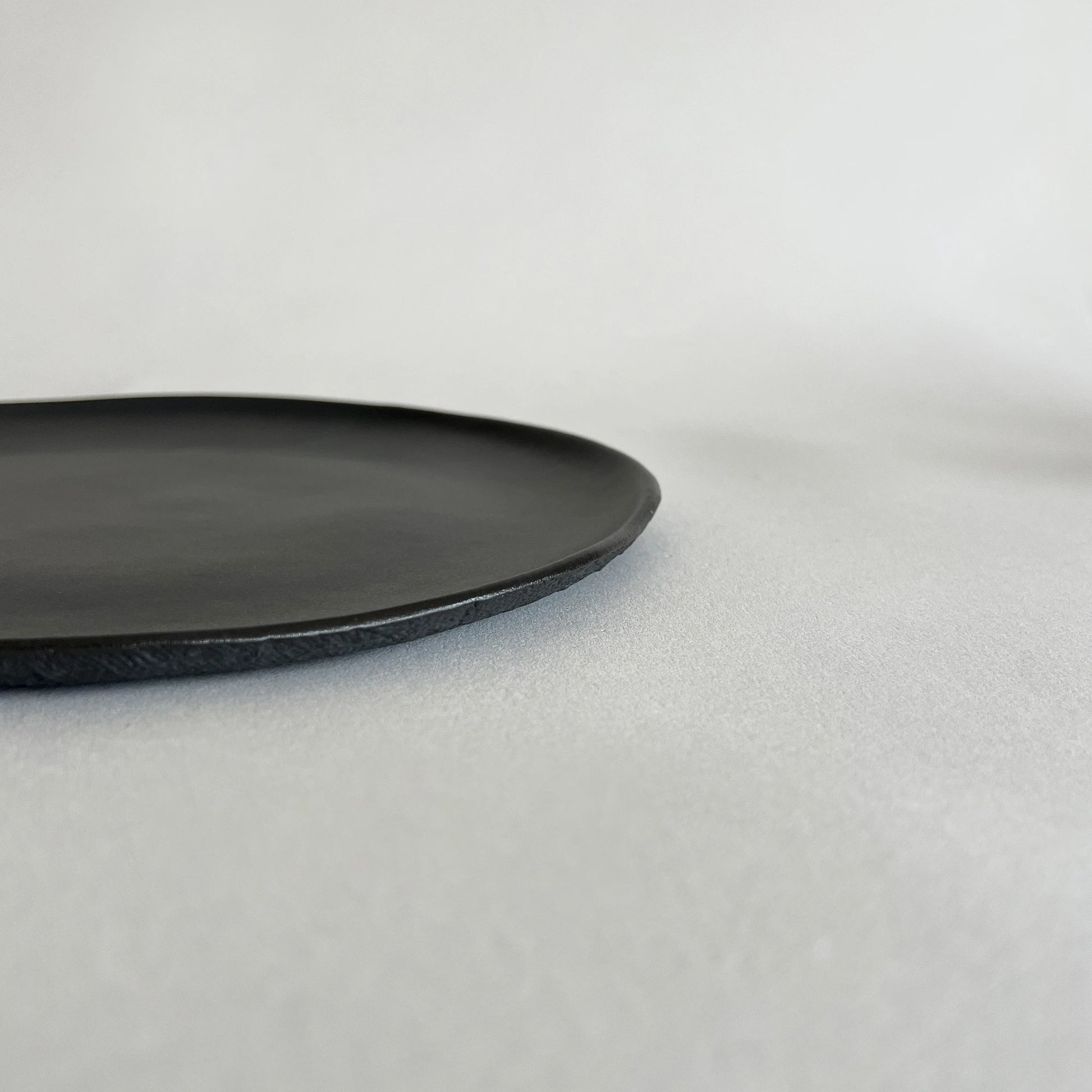 A minimalist black ceramic pizza plate with a matte finish and a slightly textured rim.