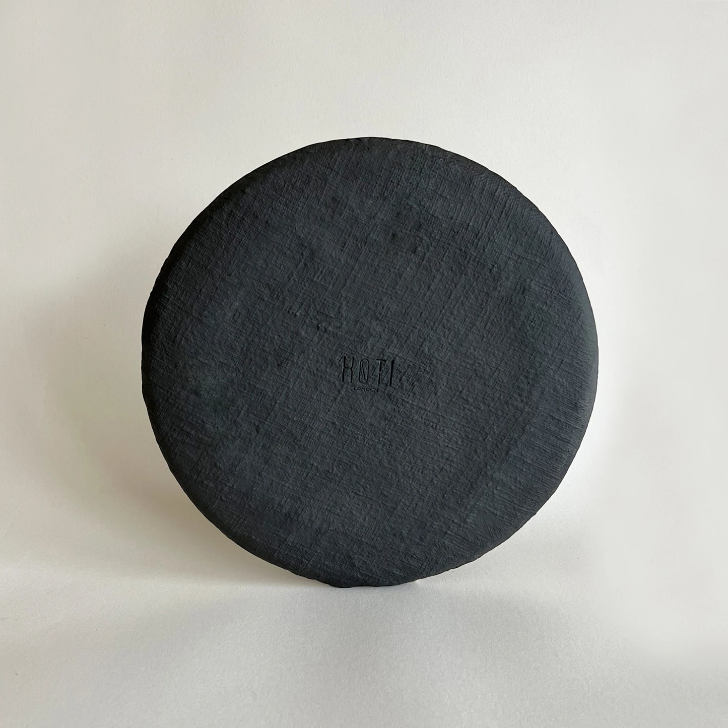 The back of a large dinner plate in matte black and satin finish, showcasing the organic textured finish. 