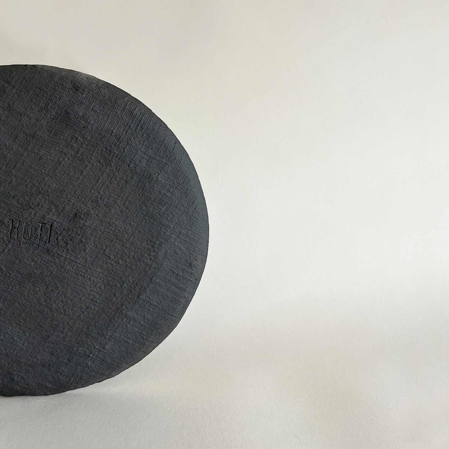 A close-up of large ceramic dinner plate in matte black satin finish, showcasing the raw textured finish. 