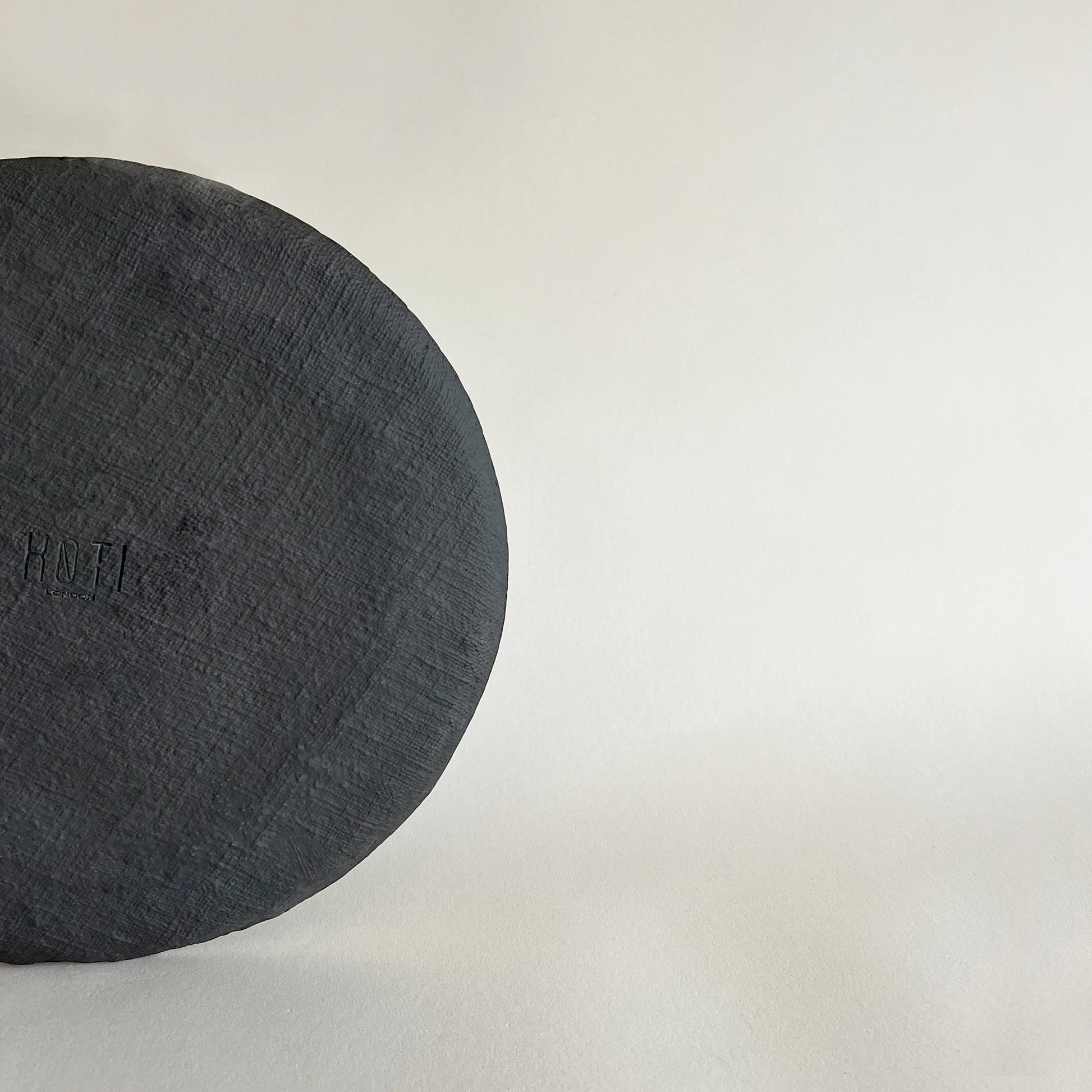 A close-up of large ceramic dinner plate in matte black satin finish, showcasing the raw textured finish. 