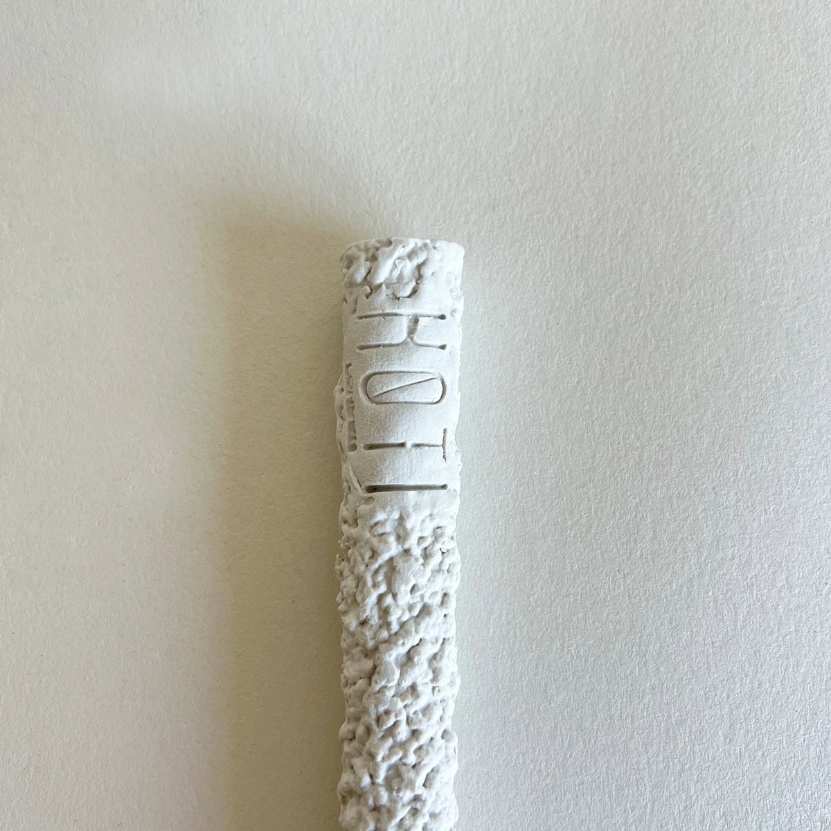 A textured white ceramic or stone close up of serving spoon handle with brand logo