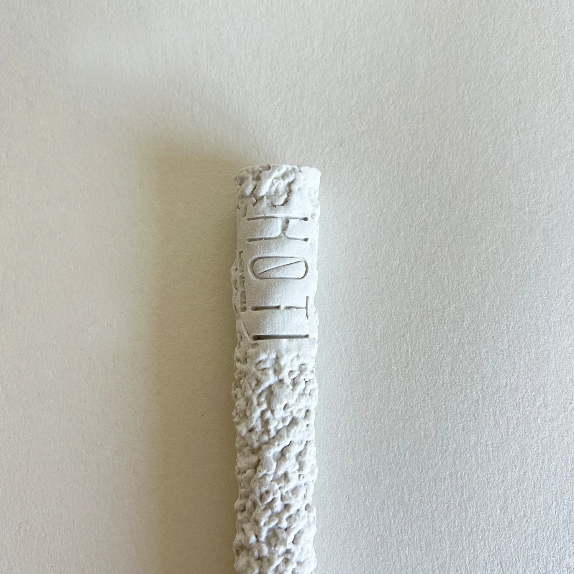 A textured white ceramic or stone close up of serving spoon handle with brand logo