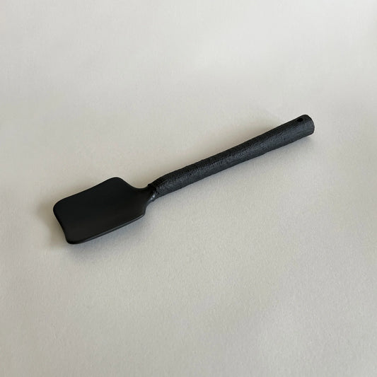 A large black matte ceramic serving spoon  with a textured black handle.
