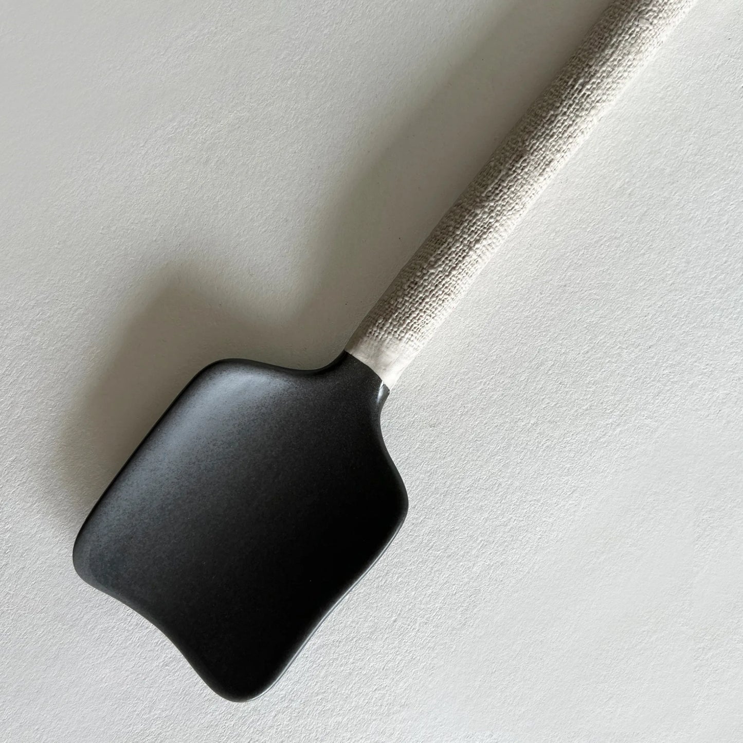 Handmade ceramic serving spoon in matte dark grey colour and contrasted woven handle.
