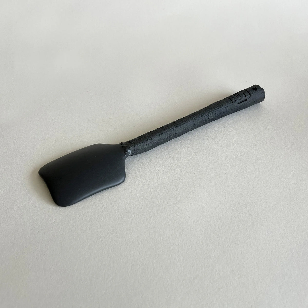 A matte black ceramic serving spoon with a textured black handle.