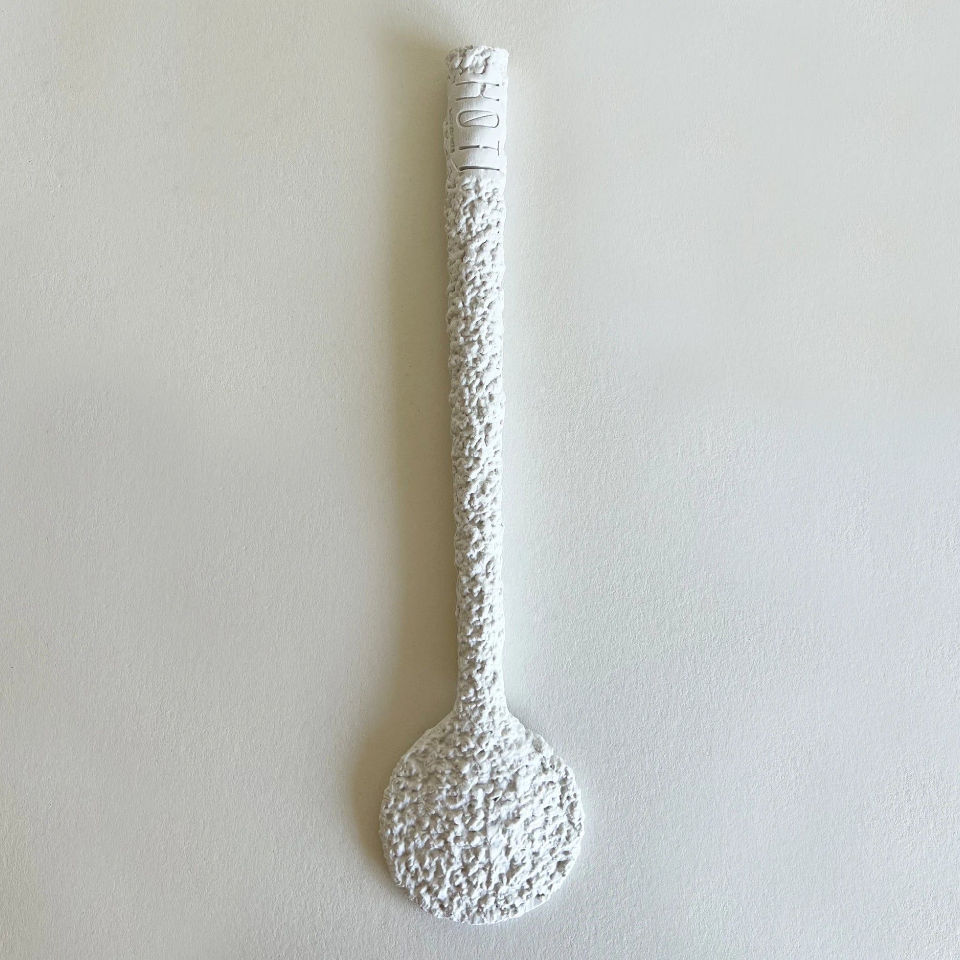 A white, textured decorative serving spoon with raw organic finish