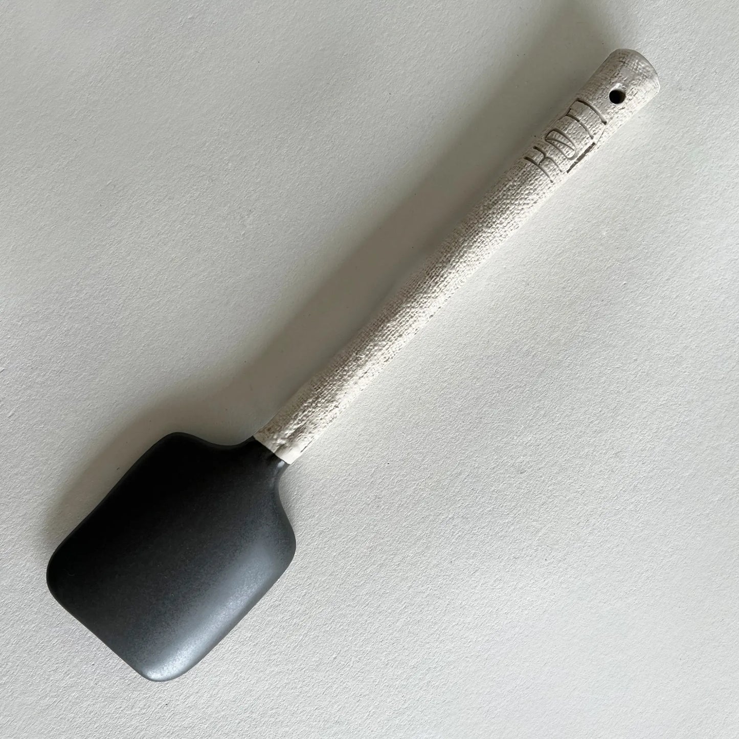 Matte dark grey and textured beige ceramic serving spoon.