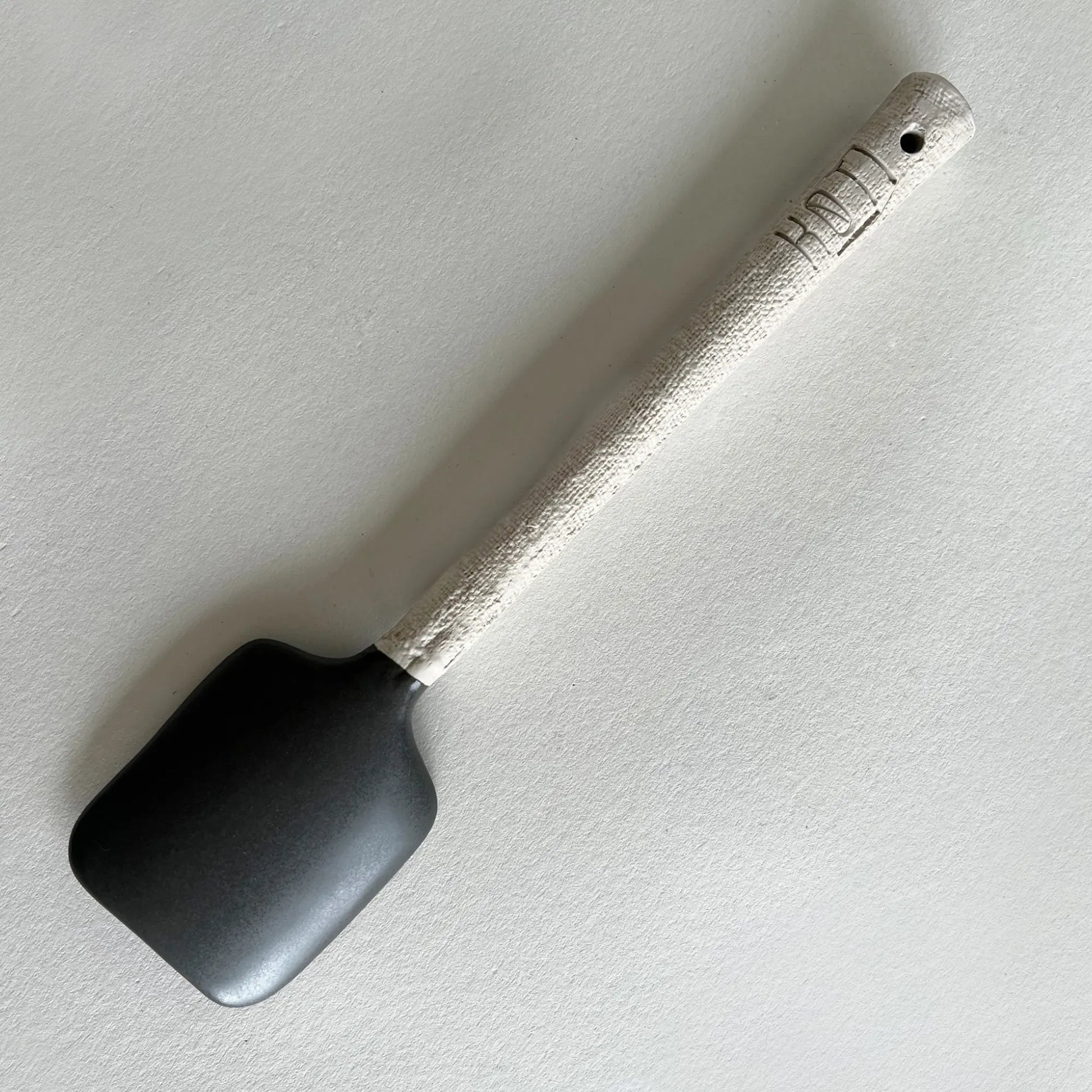 Matte dark grey and textured beige ceramic serving spoon.