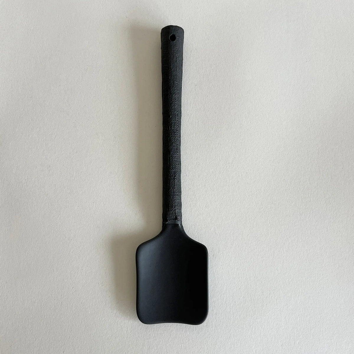 A matte black ceramic serving spoon with a textured black handle, showing the raw and organic finish. 