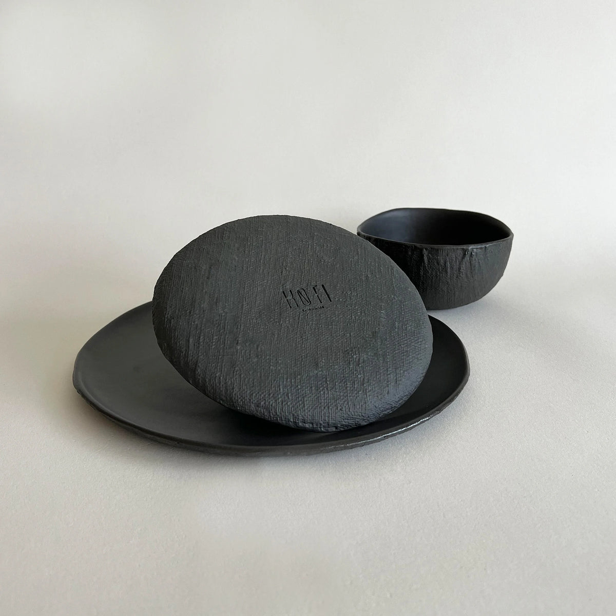 A handmade matte black ceramic set featuring a textured large dinner plate, black side plate and black breakfast bowls.