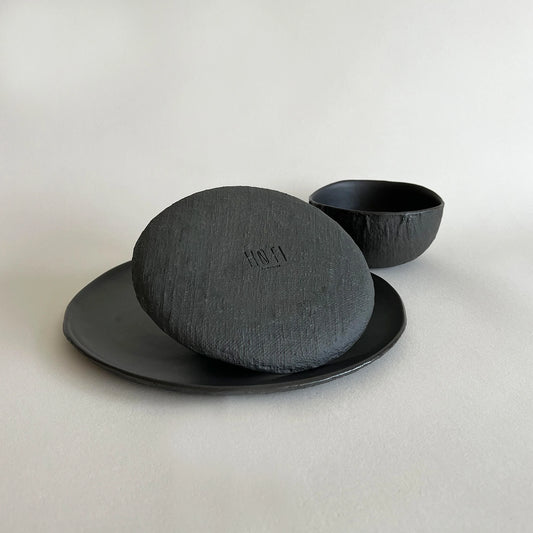 A handmade matte black ceramic set featuring a textured large dinner plate, black side plate and black breakfast bowls.