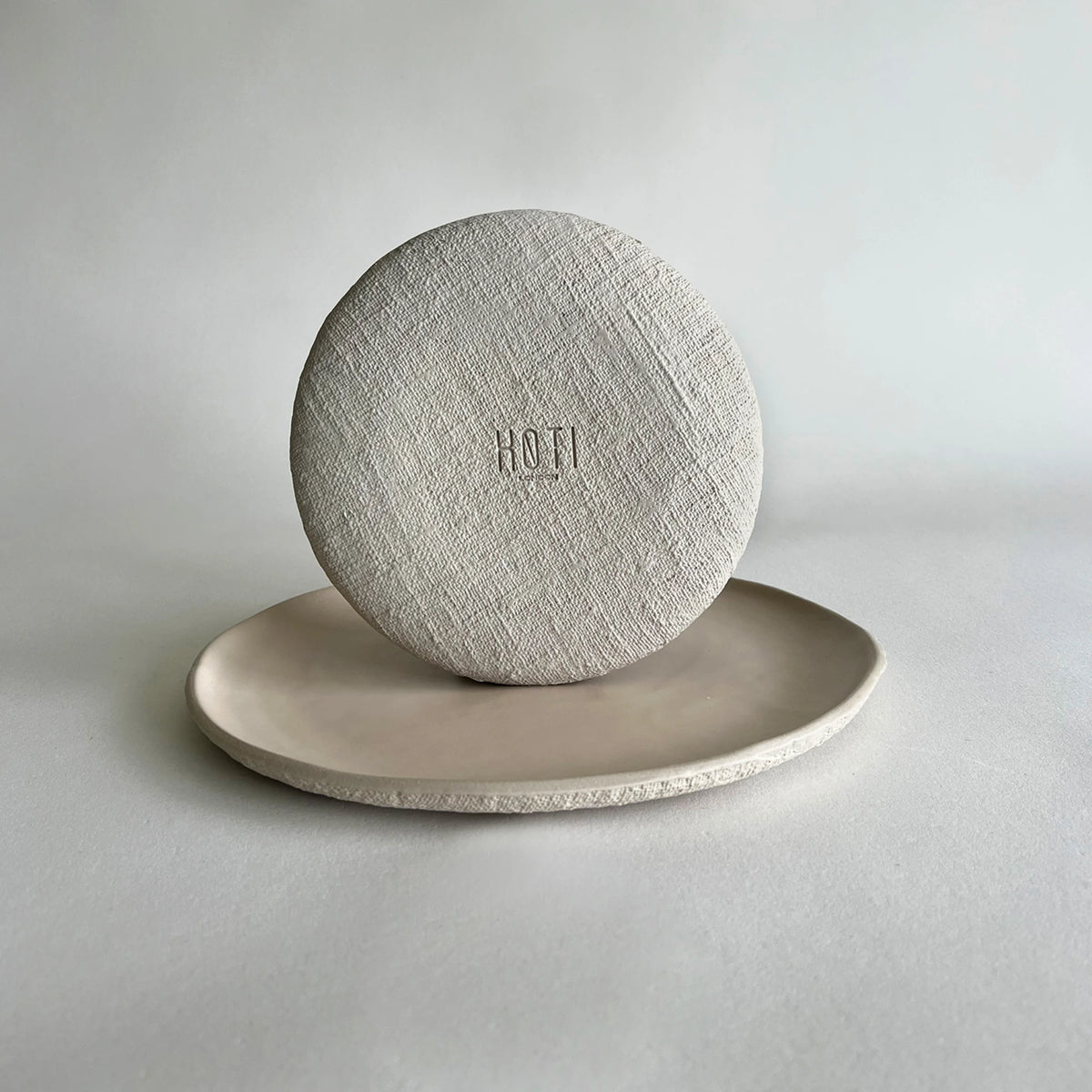 A round beige textured organic ceramic dinner plate and dessert plate showcasing the details .