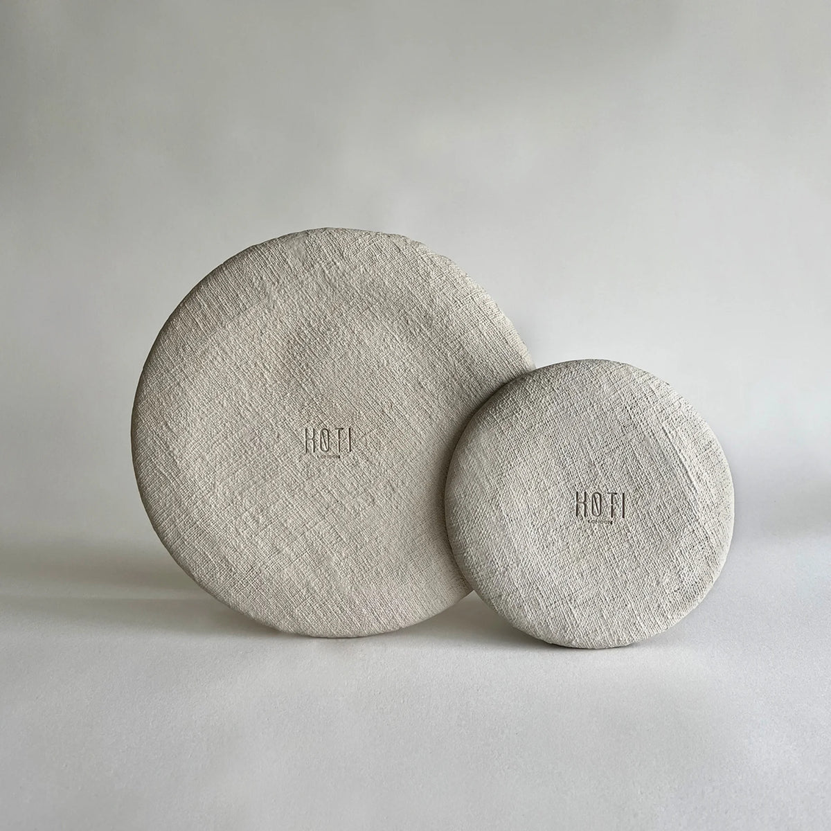 Two round textured large dinner plate and side plate in a light beige linen-like material, showcasing close up of raw organic texture with matte finish.