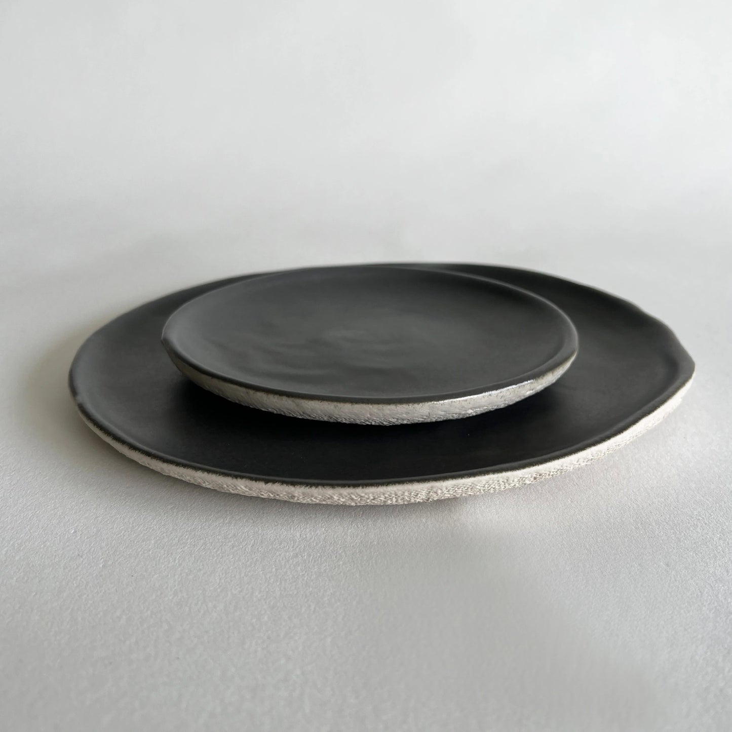 A set of two ceramic dining plate and side plate in charcoal colour with contrasted beige textured finish.