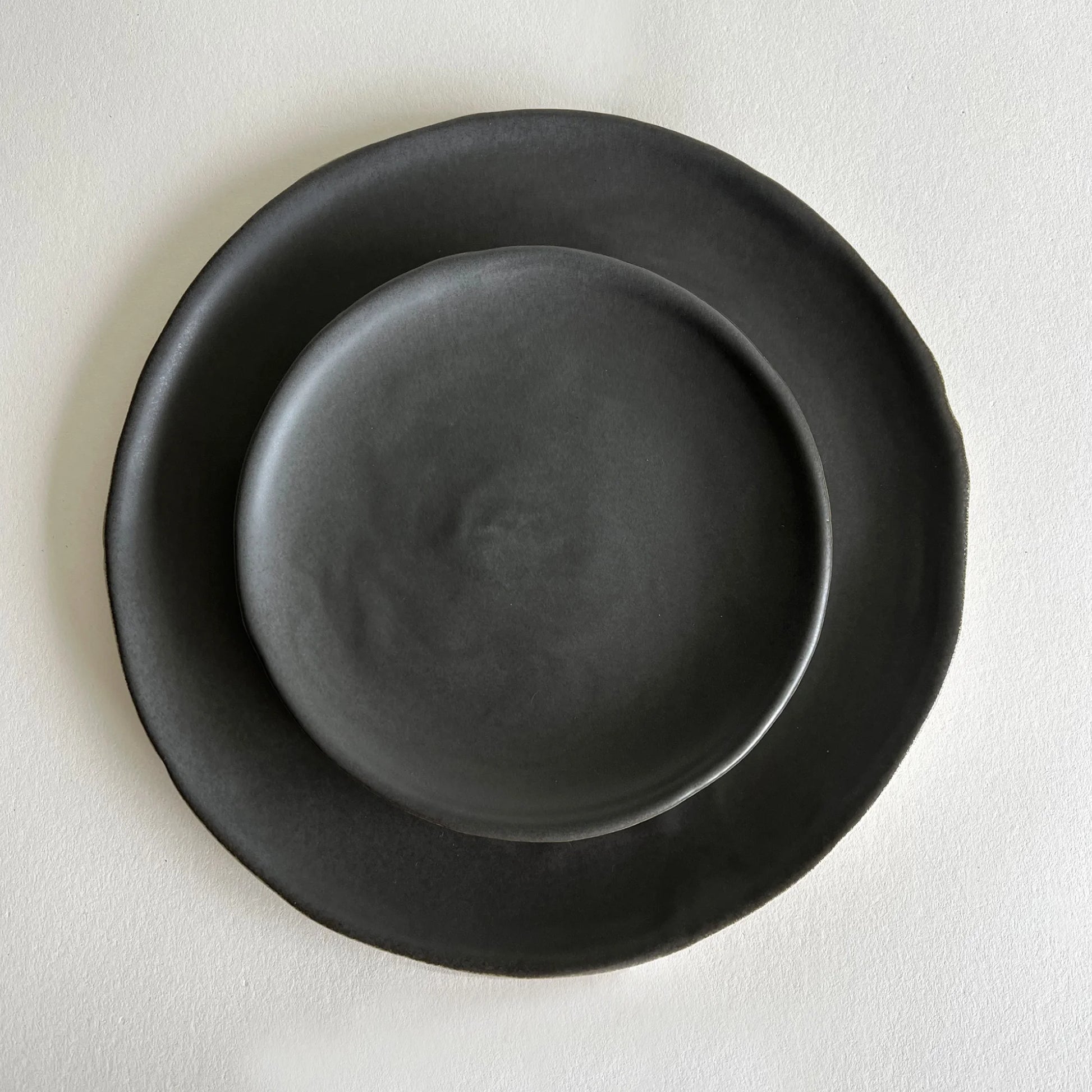 A set of two matte charcoal ceramic dinner and salad plate, organically formed.