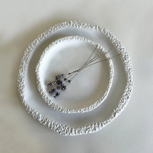 Large and dessert textured white ceramic plates with a rough, organic raised rim, styled with dried lavender sprigs on a light beige background.
