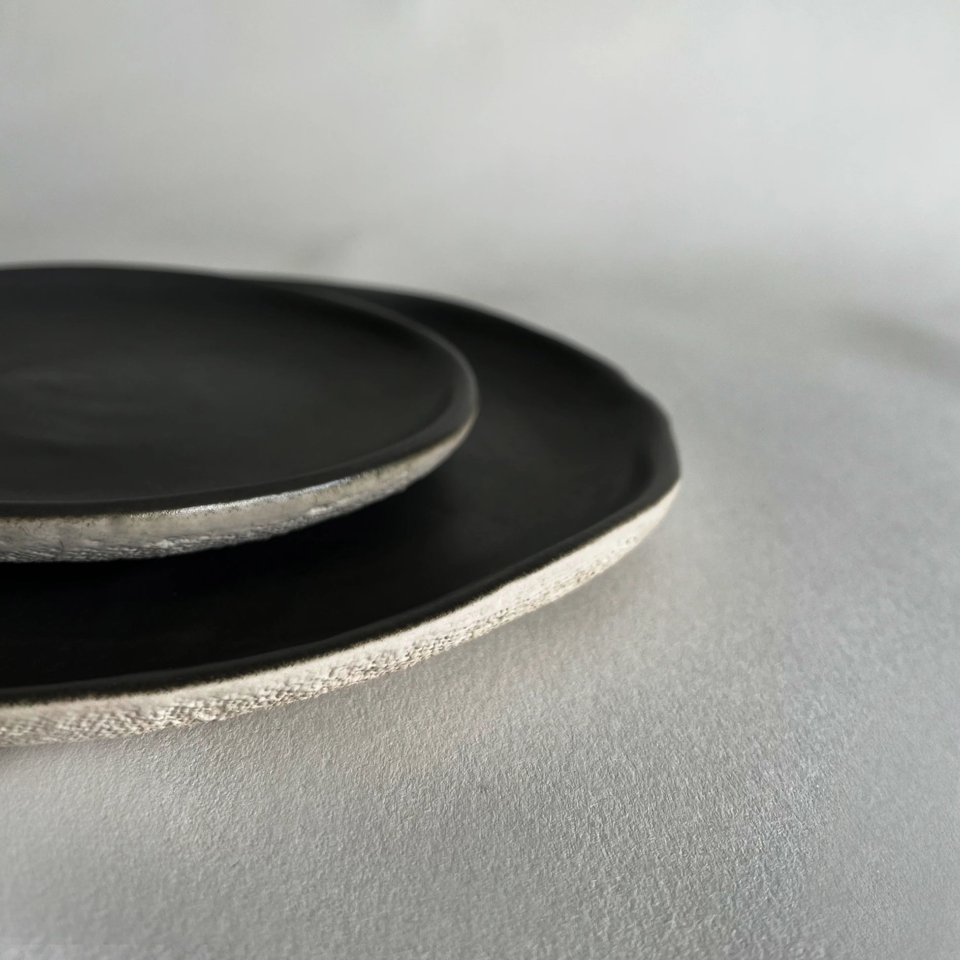 A set ow two handmade ceramic plates in matte charcoal colour, showcasing beige contrasted organic finish. 